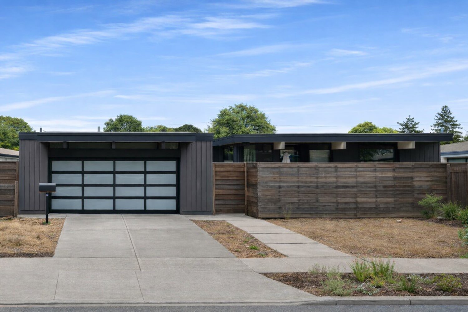 A charcoal-clad Eichler remodel in Cupertino with a frosted-glass garage door and a horizontal wood screen fence