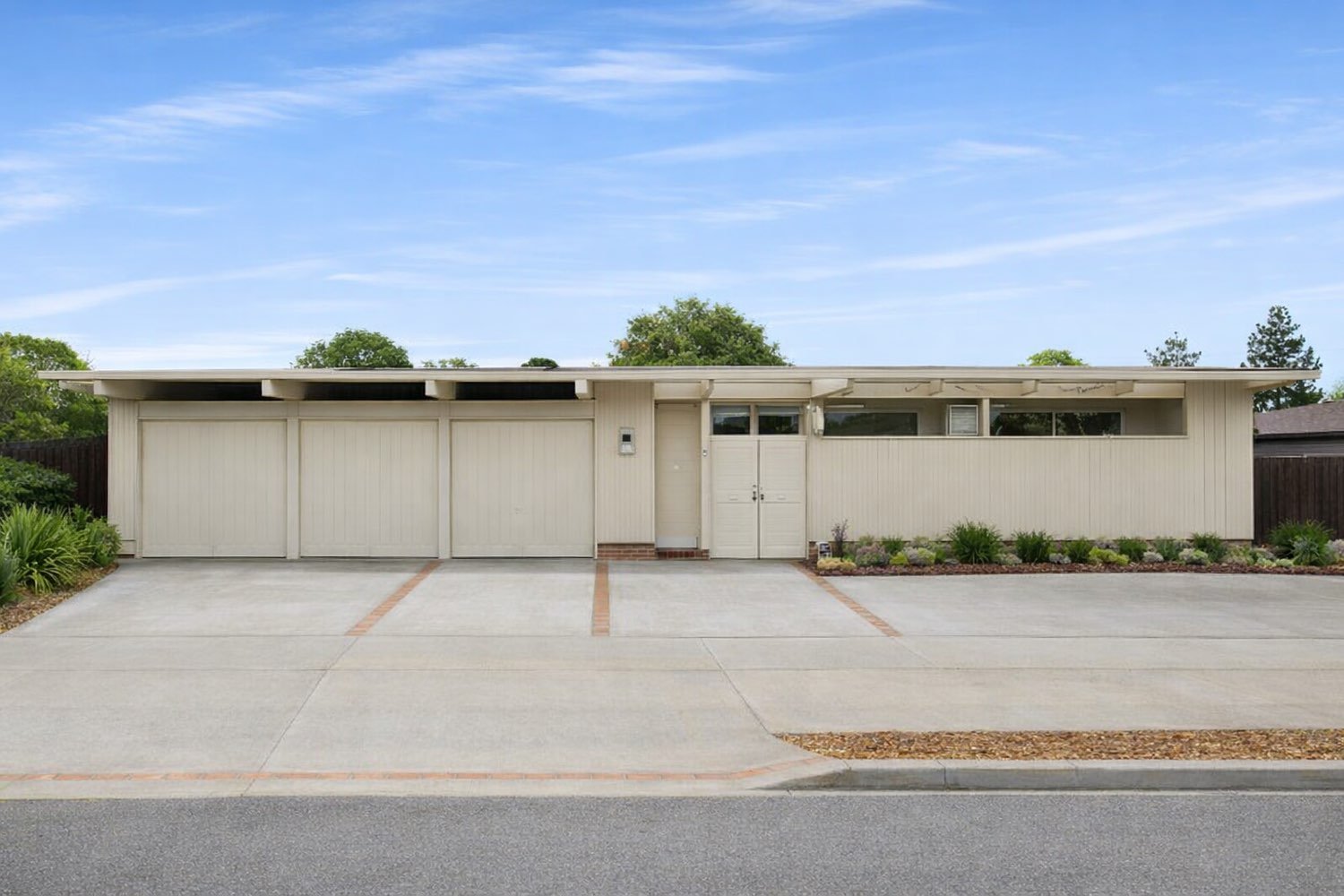 A long, low cream-painted Fairgrove Eichler with a triple garage and a clerestory window band