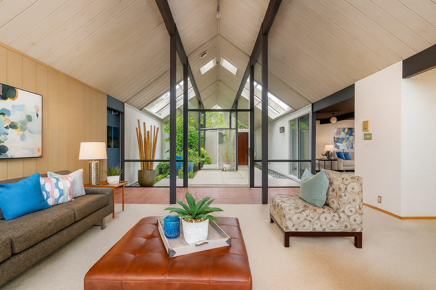 Inside an Eichler: a carpeted living room open through a wall of glass to a planted central atrium