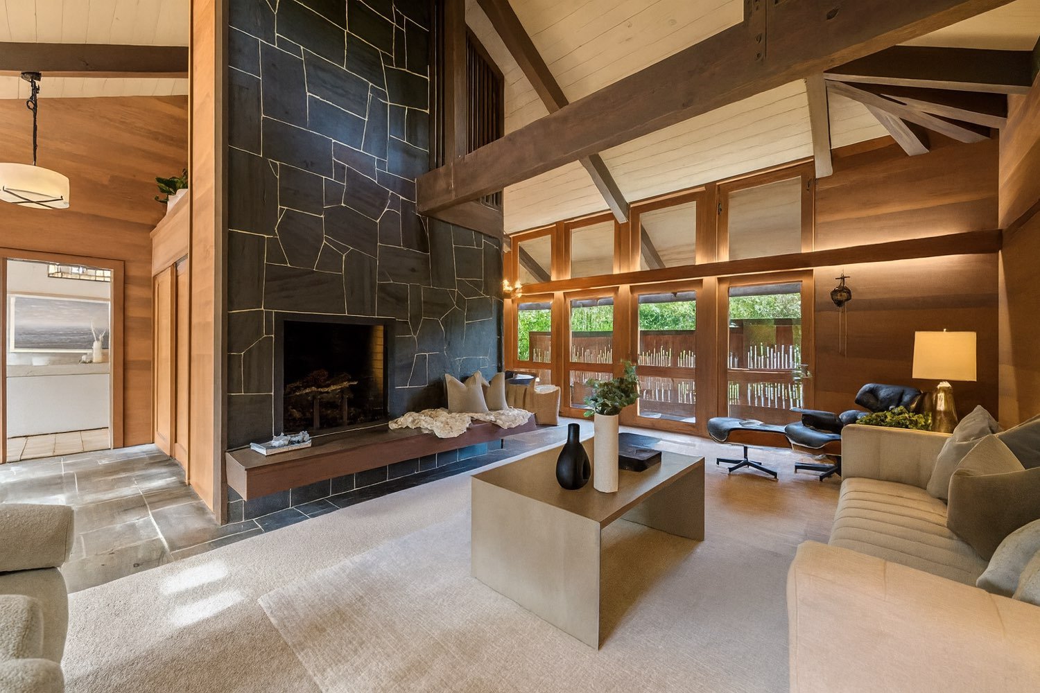 Double-height Eichler living room with a black slate fireplace wall and exposed beams